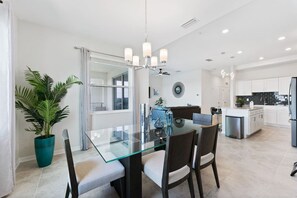 A modern kitchen with white cabinets, a central island, and a glass dining table with chairs.