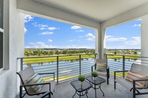 Un balcón con mobiliario exterior, vista a un cuerpo de agua y cielo despejado.
