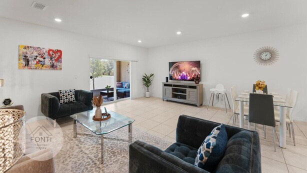 Un salón amplio con un televisor de pantalla plana grande, una zona de comedor con mesa de vidrio y un sofá moderno.