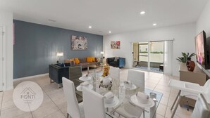Un salón amplio con una mesa de comedor dispuesta para seis personas, un sofá y un televisor.