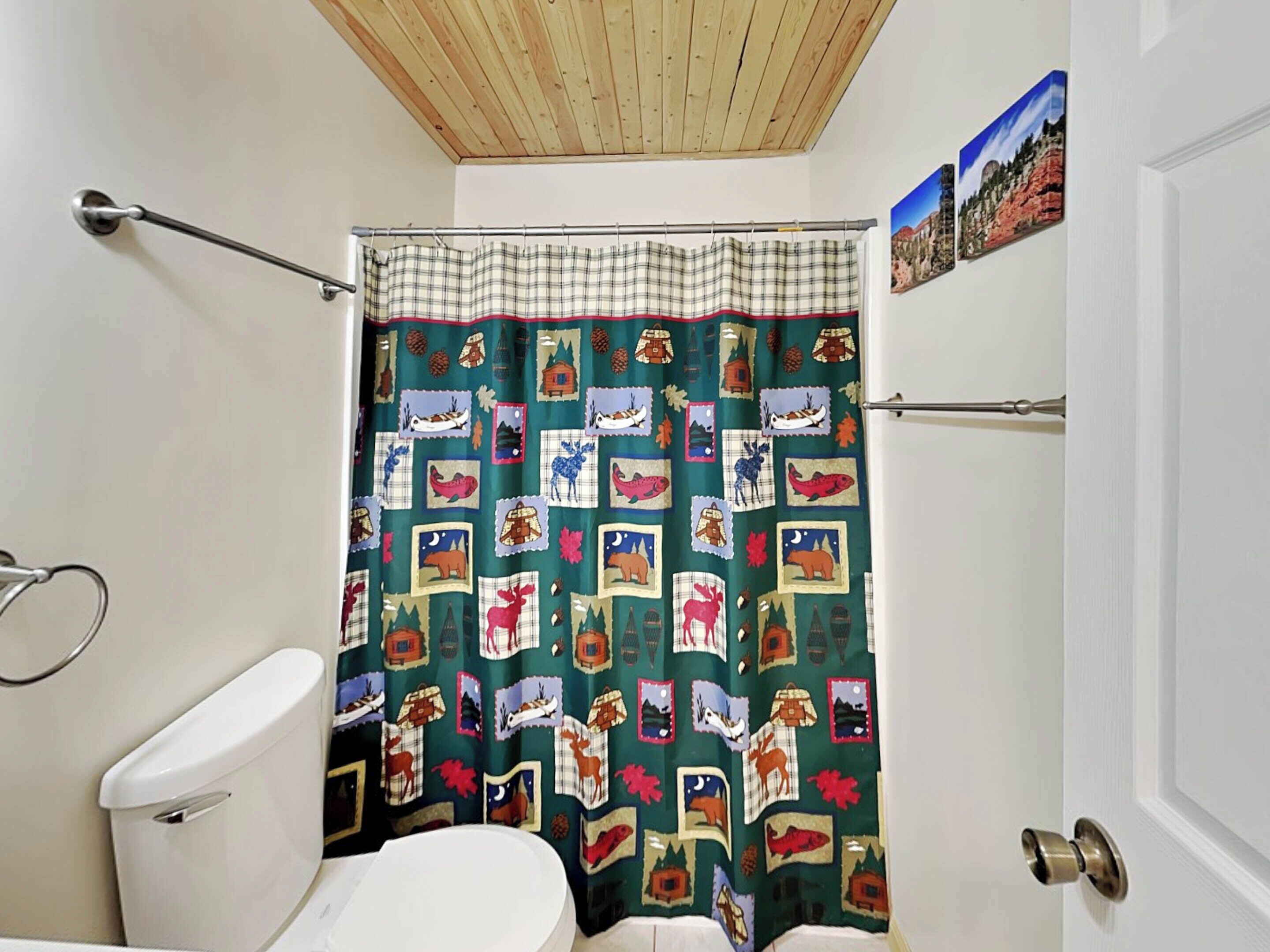 A bathroom with a plaid shower curtain, a toilet, and a door with a picture on the wall.