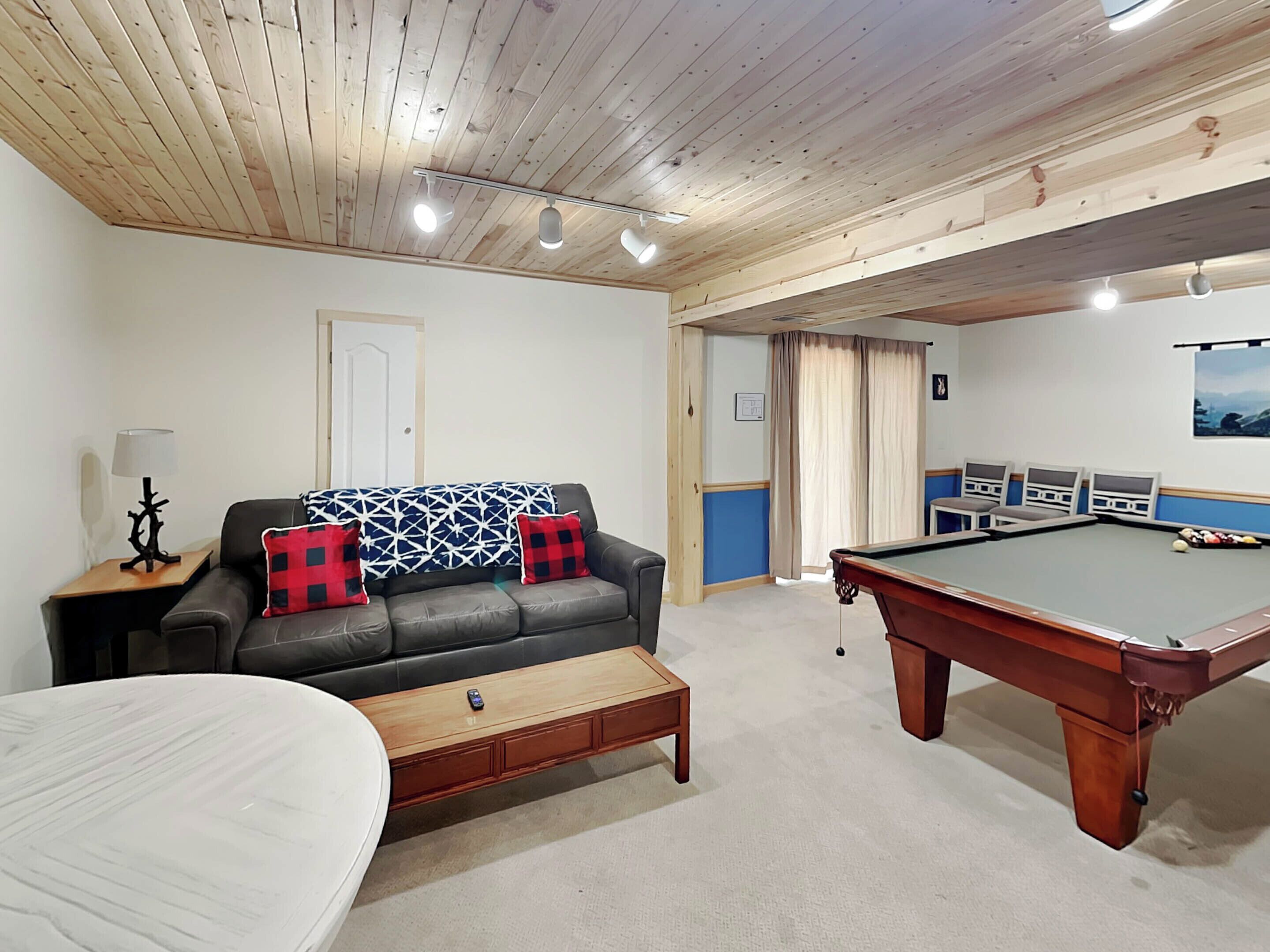 A room with a pool table, a sofa with patterned cushions, a lamp, and a bed.