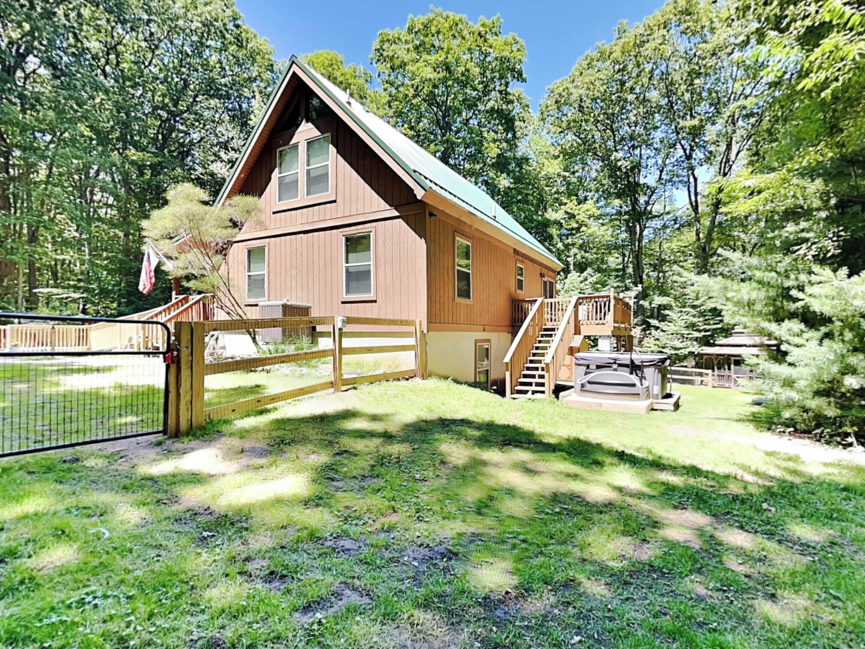 A wooden cabin with a green roof, surrounded by trees and a fenced yard.