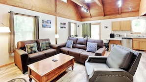 Ein geräumiges Wohnzimmer mit hoher Decke, Holzbalken, Deckenventilator und einem Essbereich, im Hintergrund ist eine Küche zu sehen.