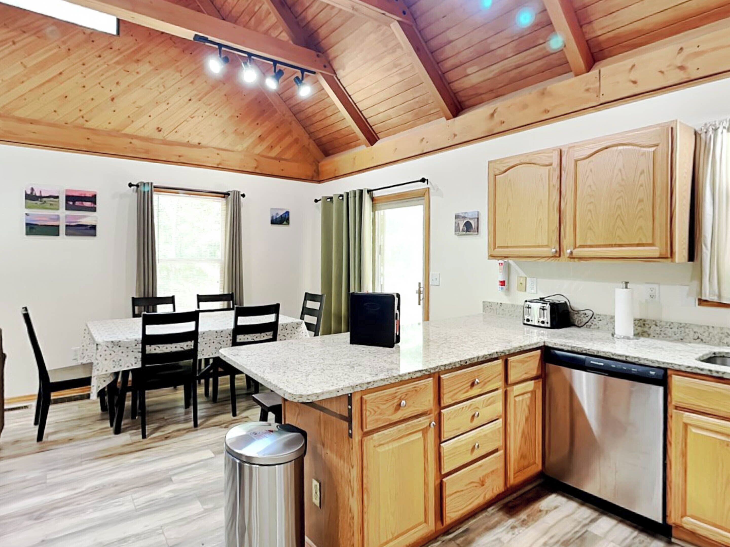 A kitchen with wooden cabinets, a granite countertop, a dishwasher, and a dining area with a table and chairs.