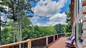 A wooden deck with a railing, a seating area with chairs, and a view of trees and sky. - Sunset Bluff by Taylor Made Deep Creek (McHenry)