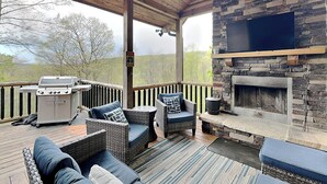 A covered deck with wicker furniture, a grill, and a stone fireplace. - Sunset Bluff by Taylor Made Deep Creek (McHenry)