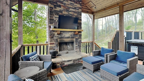 A covered outdoor seating area with wicker furniture, a stone fireplace, and a TV mounted on the wall. - Sunset Bluff by Taylor Made Deep Creek (McHenry)