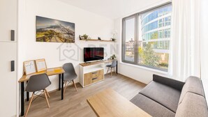 Een moderne woonkamer met een houten bureau, twee stoelen, een bank, een televisie en een groot raam met uitzicht op de stad.