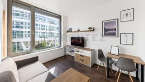 Un salon moderne doté d’une grande fenêtre, d’un téléviseur à écran plat, d’un bureau en bois, de deux chaises et d’un canapé.