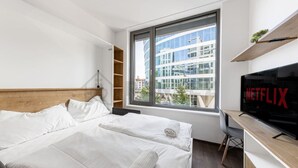 Une chambre d’hôtel moderne dotée d’un grand lit, d’un bureau avec une télévision et d’une fenêtre donnant sur la ville.
