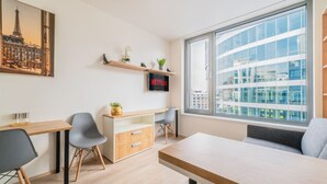 Ein modernes Zimmer mit Schreibtisch, Stühlen, einem großen Fenster mit Stadtblick, einem Regal mit Pflanzen und einem Netflix-Schild.