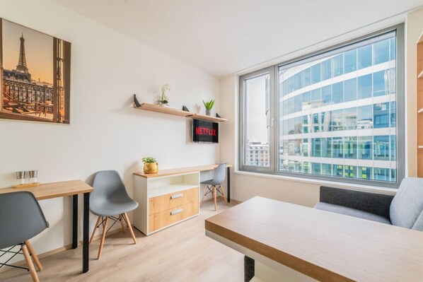 A modern room with a desk, chairs, a large window with a city view, a shelf with plants, and a Netflix sign.