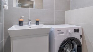 Ein modernes Badezimmer mit einem weißen Waschbecken, einem Spiegel und einer Waschmaschine mit Frontlader.