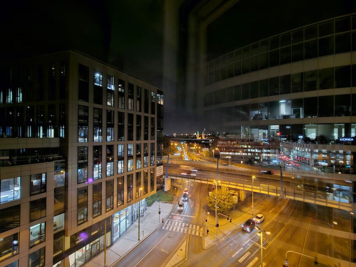 Un paisaje urbano nocturno con edificios modernos, un cruce con mucho tráfico y calles iluminadas.