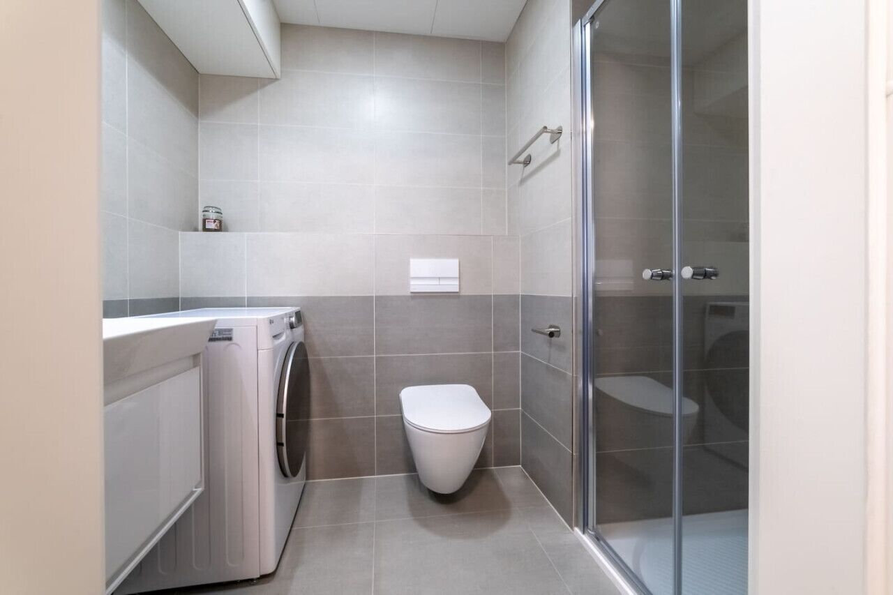 Baño pequeño con lavadora, inodoro y cabina de ducha de vidrio.