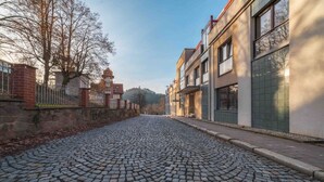 A cobblestone street with buildings on either side, a stone wall on the left, and a clear sky.