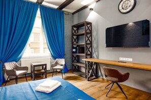Ein Hotelzimmer mit einem Bett, zwei Stühlen, einem Schreibtisch, einem Fernseher und einem Bücherregal.