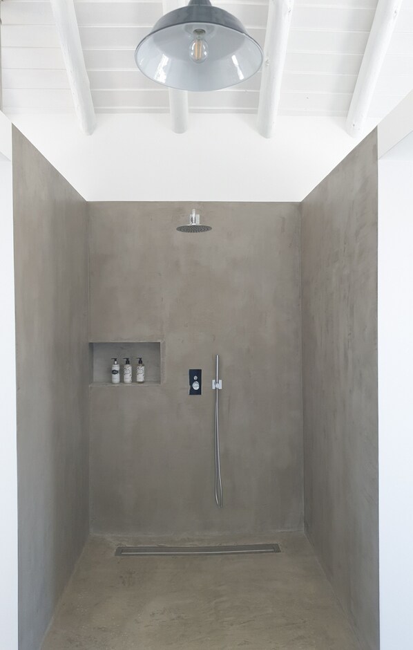 A modern shower room with a concrete wall, a ceiling light, and a control panel.