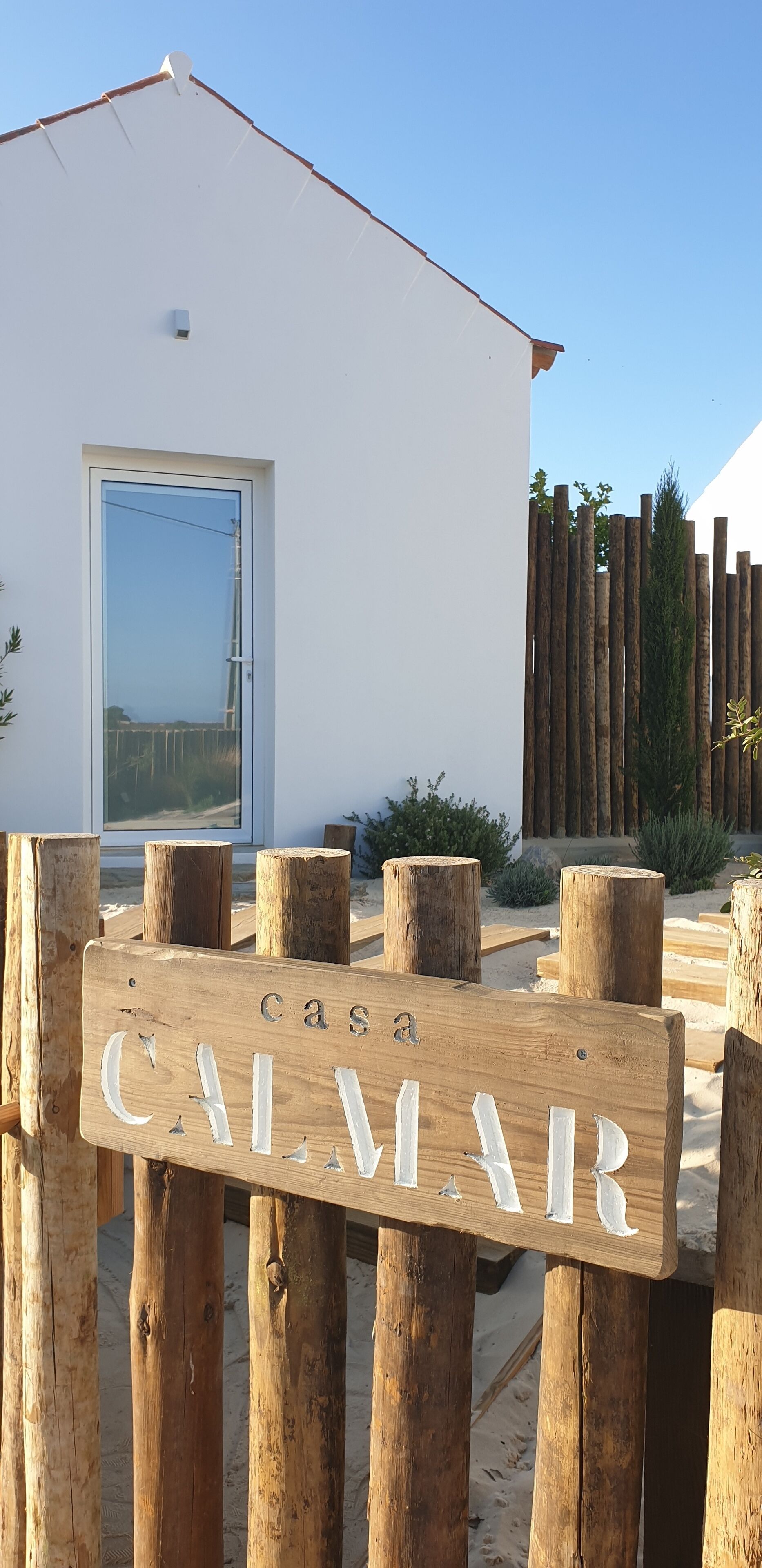 Uma placa de madeira com o nome 'CASA CALMAR' em frente a um edifício branco com porta de vidro.
