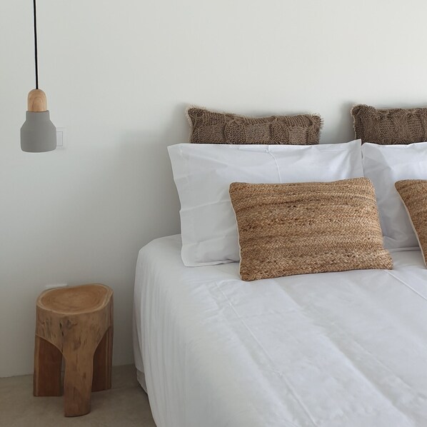 A neatly made bed with white bedding and three textured pillows.