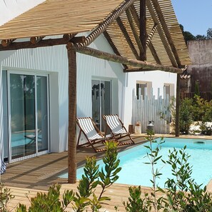 A modern villa with a pool, wooden deck, and two lounge chairs.