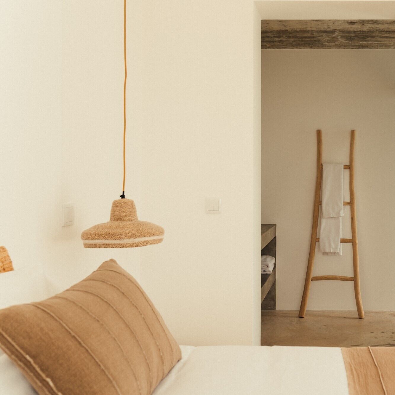 A bedroom with a bed, a hanging light fixture, and a wooden ladder against the wall.