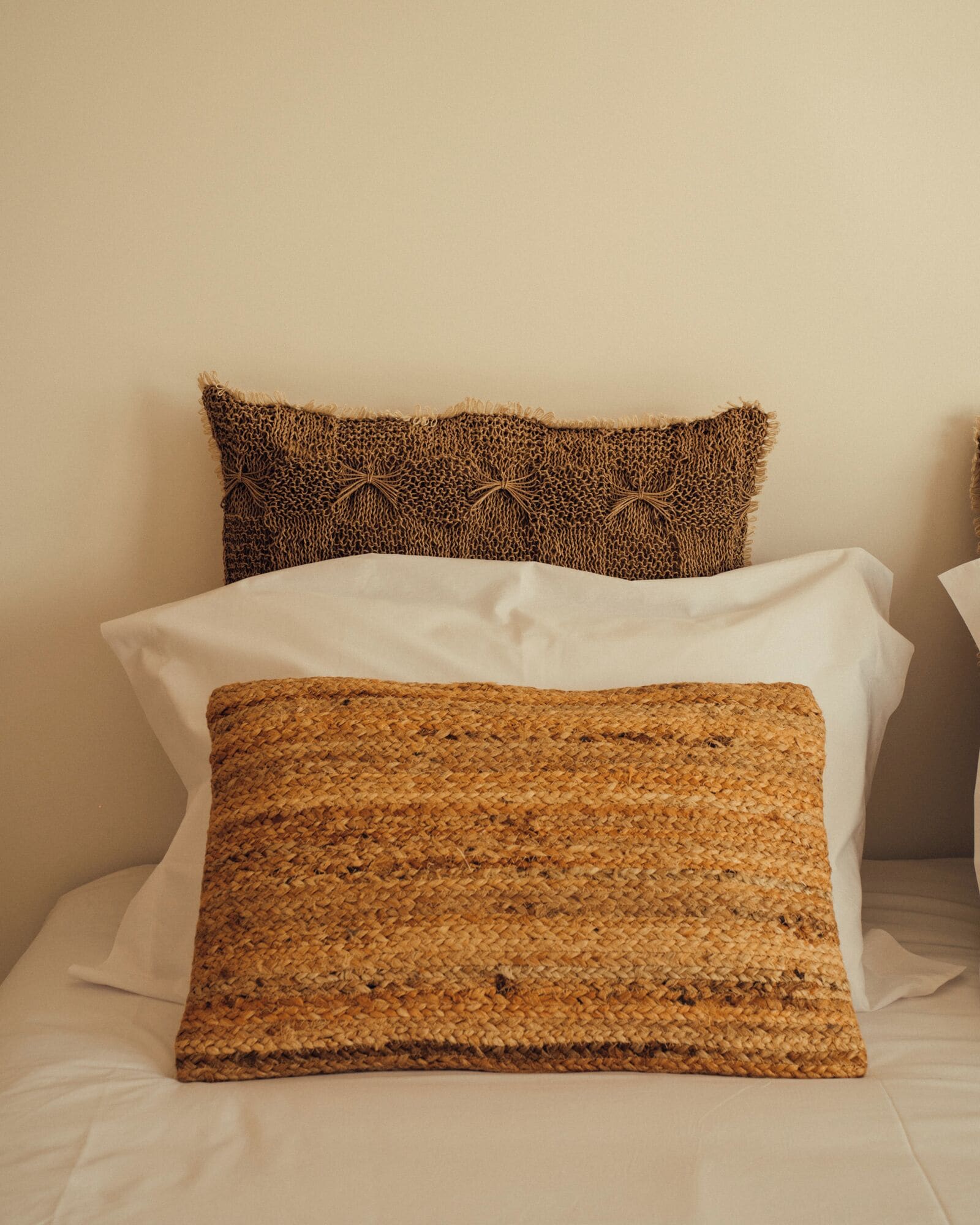 A bed with three pillows: two with a textured, woven pattern and one with a smooth, white surface.