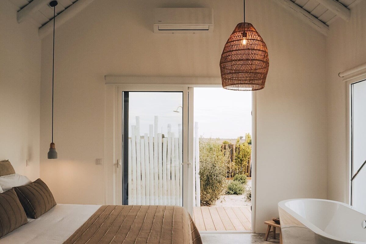 A bedroom with a bed, a hanging light fixture, a sliding glass door leading to an outdoor area, and a bathtub.