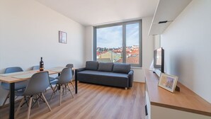 Un salon moderne comprenant un canapé, une table à manger, des chaises et une grande fenêtre donnant sur la ville.