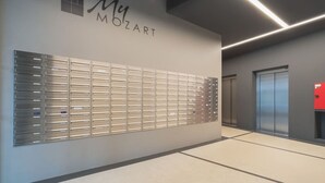 Un couloir moderne avec un meuble de rangement en métal, une plaque fixée au mur portant l’inscription « My MOZART », et un ascenseur.