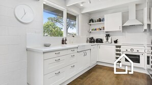 A modern kitchen with white cabinetry, a built-in oven, and a window overlooking greenery. - Blairgowrie Back Beach Holiday Escape (Blairgowrie)