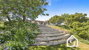 A set of wooden steps leading to a house with a porch, surrounded by lush greenery and flowering plants. - Blairgowrie Back Beach Holiday Escape (Blairgowrie)