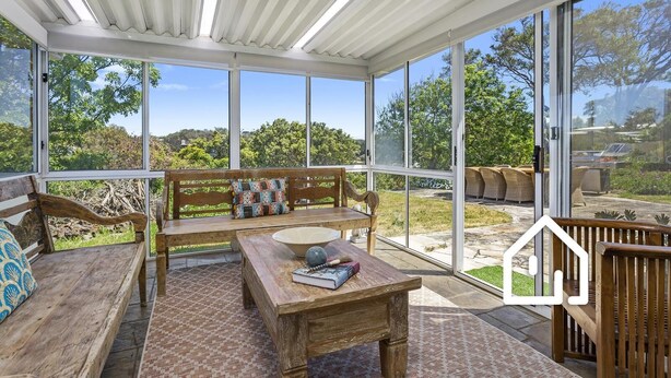 A sunroom with large windows, a wooden bench, a table, and wicker furniture. - Blairgowrie Back Beach Holiday Escape (Blairgowrie)