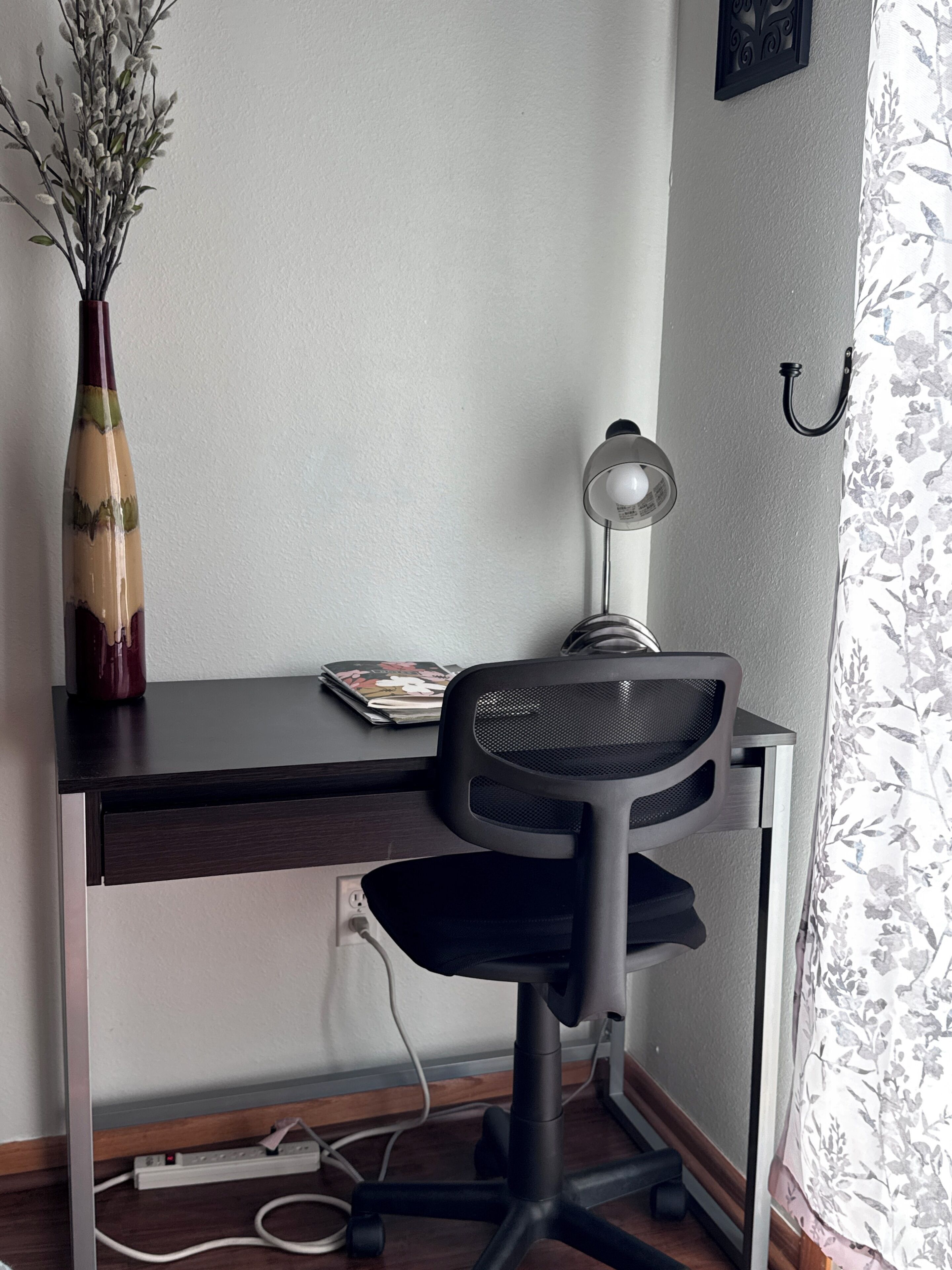Un bureau avec une chaise, une lampe et un vase décoré de branches.
