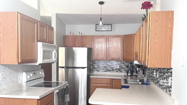 A compact kitchen with wooden cabinets, a stainless steel refrigerator, a microwave, and a stove. - Cozy and Charming Amber Valley Haven in Fargo (Fargo)