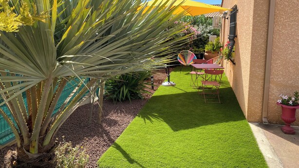Een tuin met kunstgras, een palmboom en tuinmeubilair.