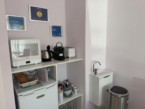 Eine Küchenzeile mit Mikrowelle, Toaster, Wasserkocher und Kaffeemaschine auf einer weißen Arbeitsplatte. An der Wand oberhalb der Arbeitsplatte befinden sich gerahmte Auszeichnungen.