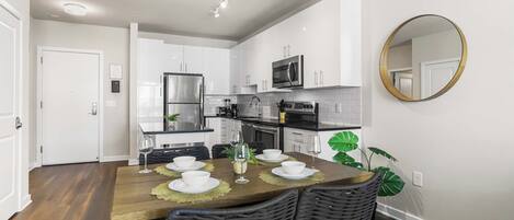 A modern kitchen with white cabinets, stainless steel appliances, and a dining area with a wooden table and wicker chairs.