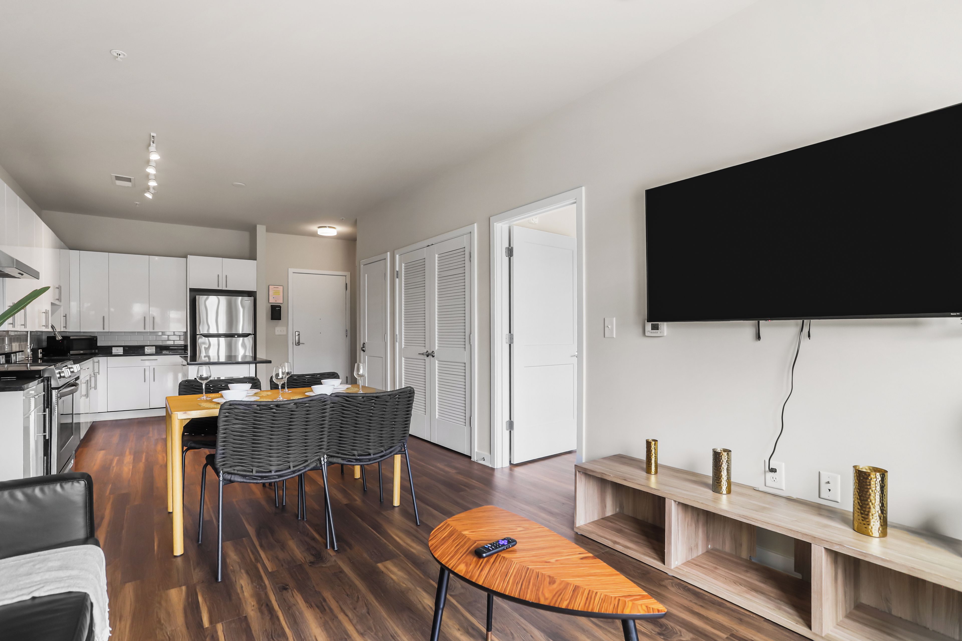 A modern kitchen with white cabinets, a stainless steel refrigerator, and a dining area with a wooden table and chairs.