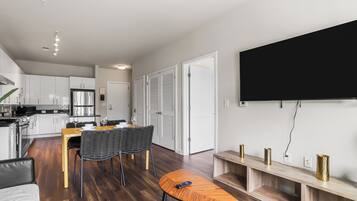 A modern kitchen with white cabinets, a stainless steel refrigerator, and a dining area with a wooden table and chairs.