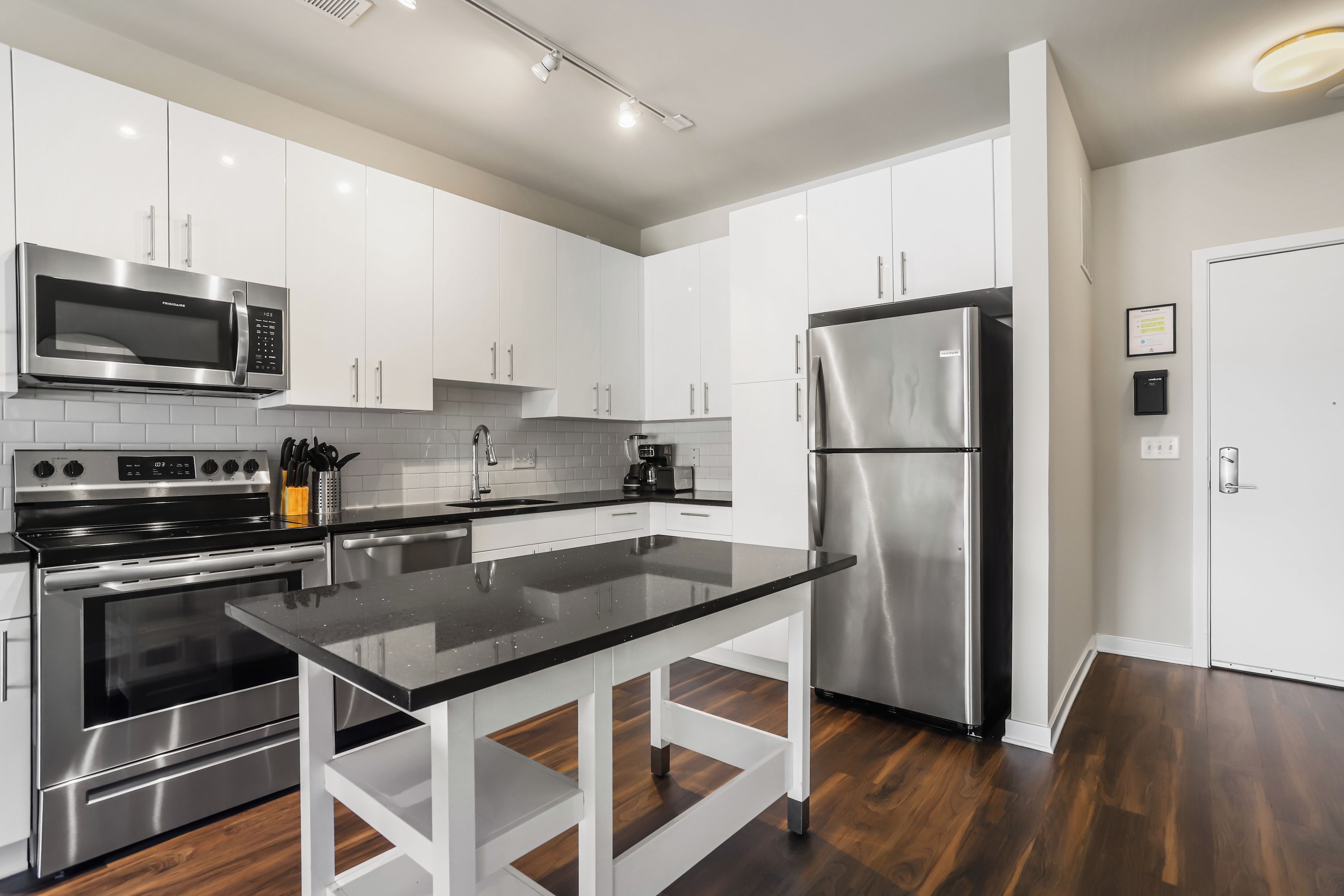 A modern kitchen with stainless steel appliances, white cabinetry, and a black countertop.