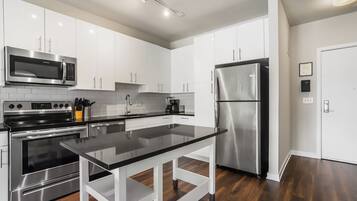A modern kitchen with stainless steel appliances, white cabinetry, and a black countertop.