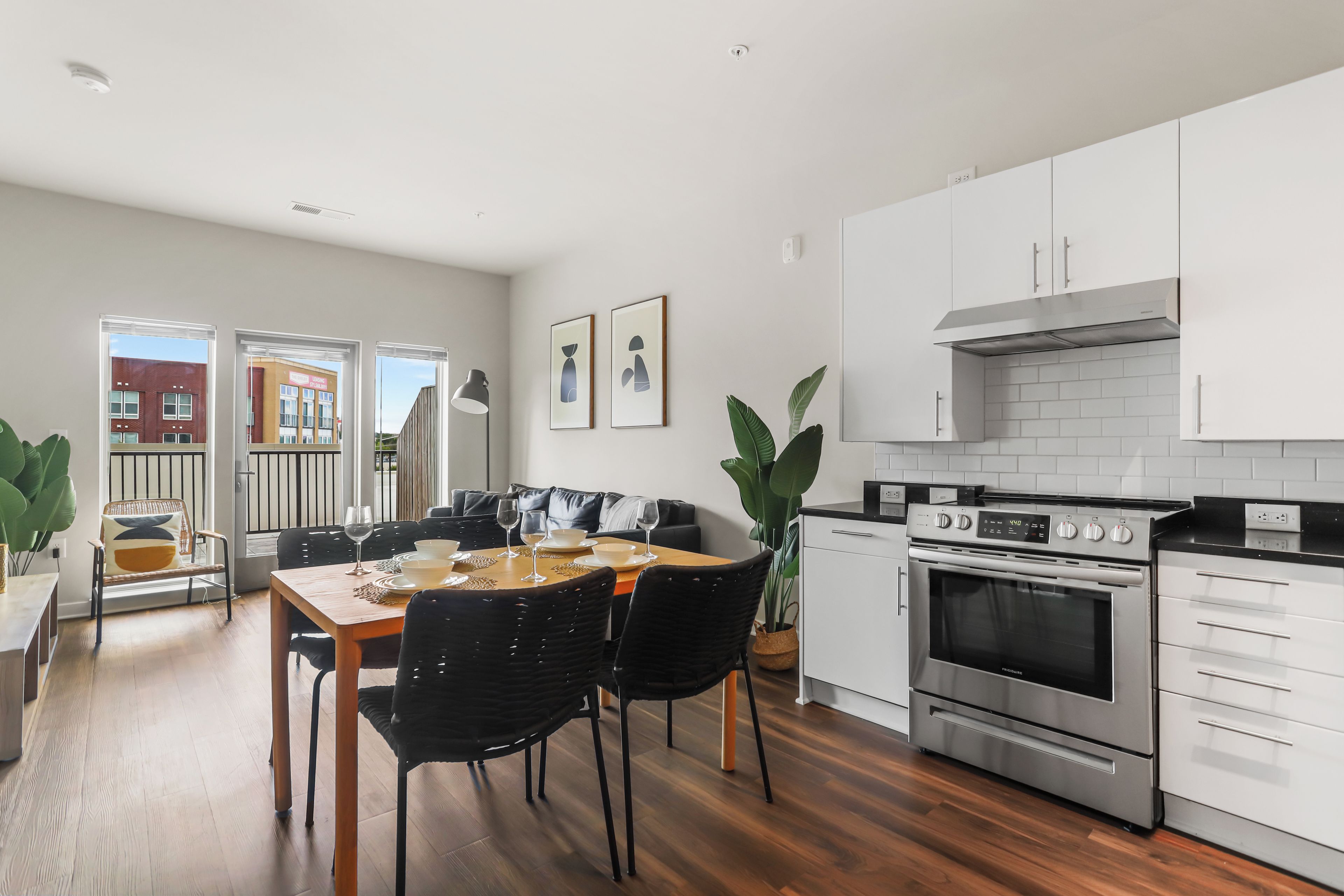 Una cocina moderna con armarios blancos, horno de acero inoxidable y comedor con mesa de madera y sillas negras.