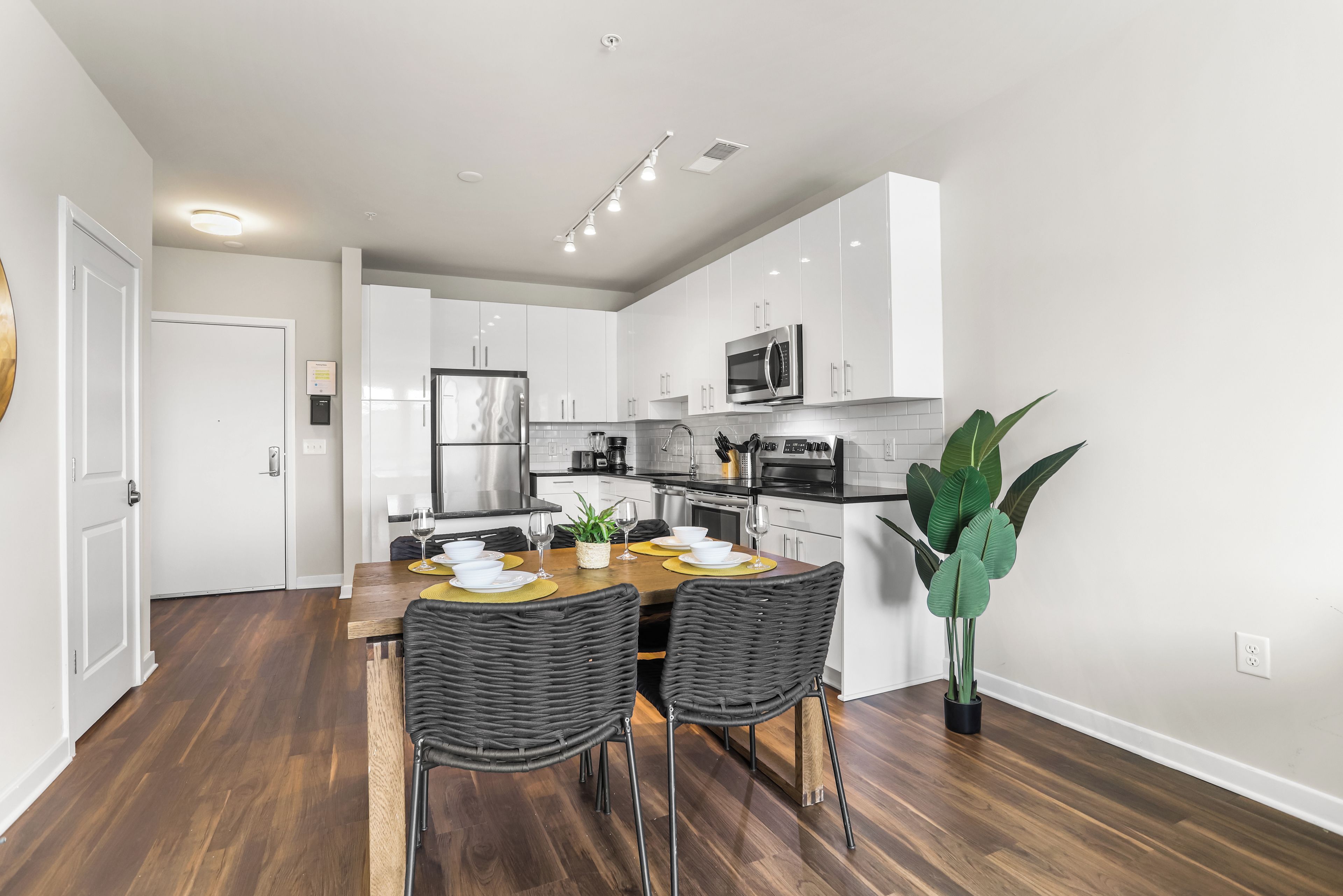 A modern kitchen with white cabinets, stainless steel appliances, and a dining area with a wooden table and wicker chairs.