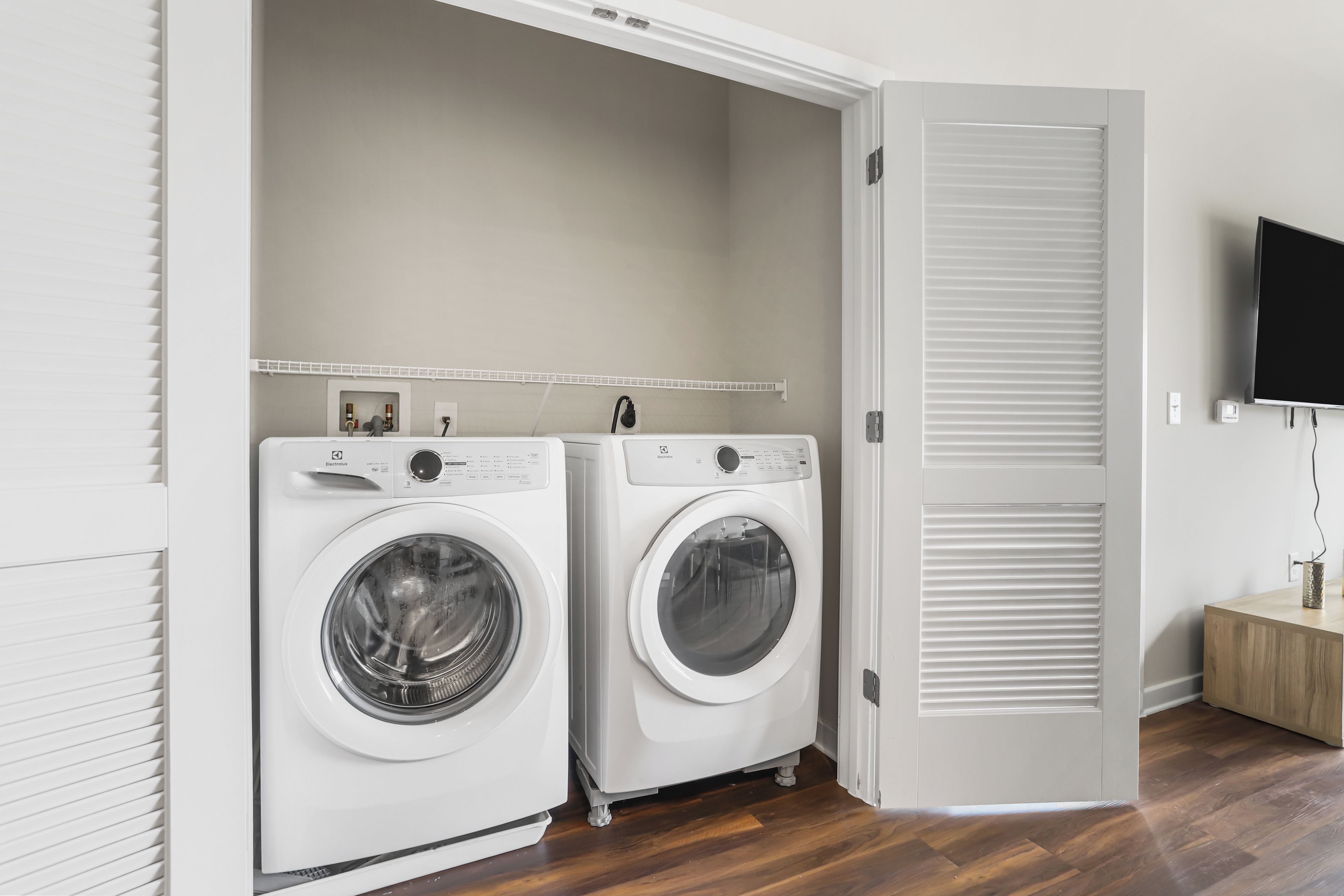 A laundry room with two front-loading washing machines, a wooden floor, and a white door with a sliding closet.