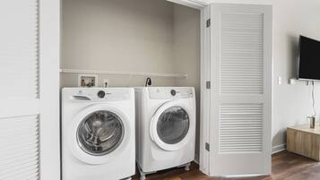 A laundry room with two front-loading washing machines, a wooden floor, and a white door with a sliding closet.
