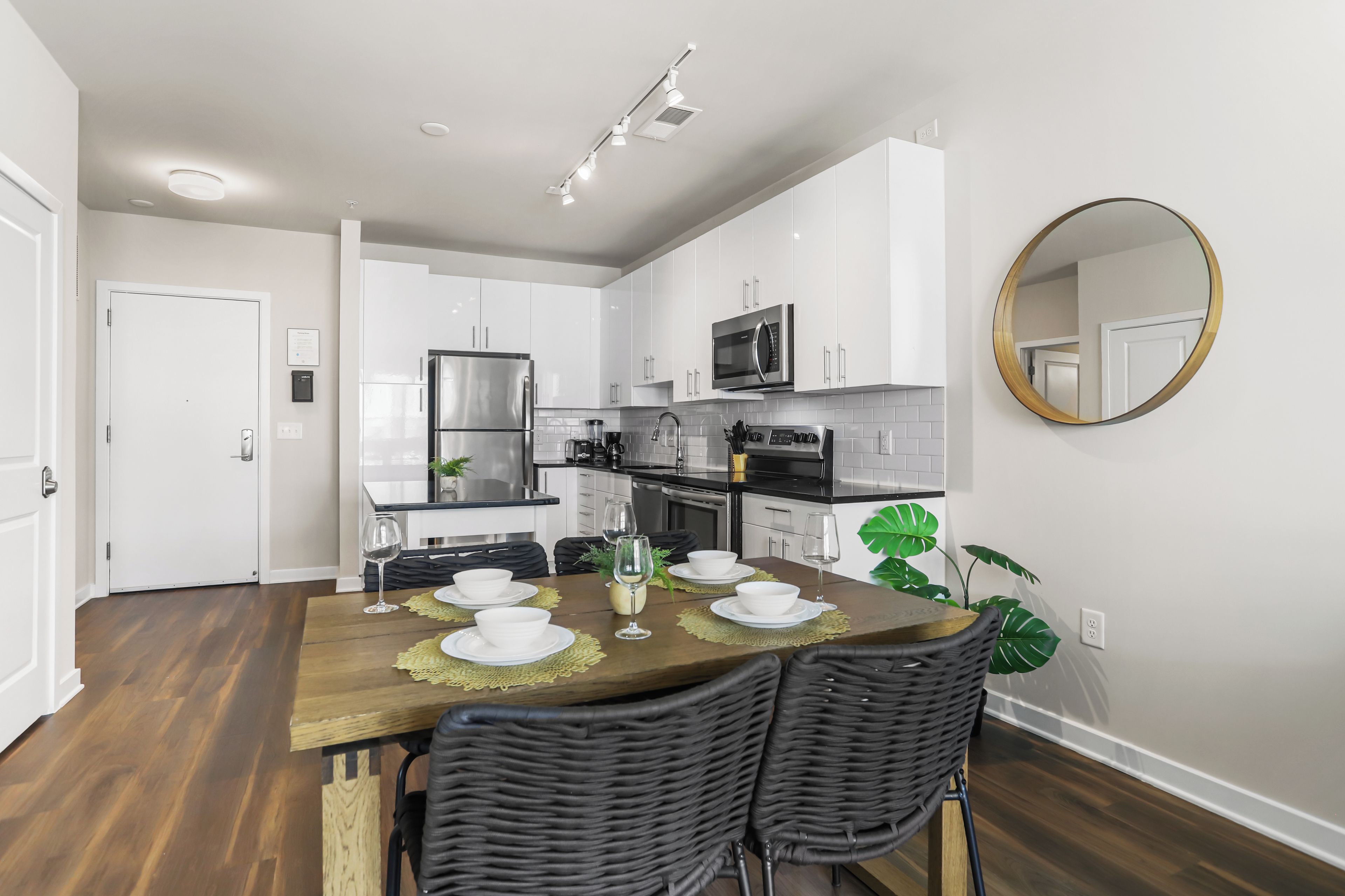 A modern kitchen with white cabinets, a stainless steel refrigerator, a microwave, and a dining area with a wooden table set for four.