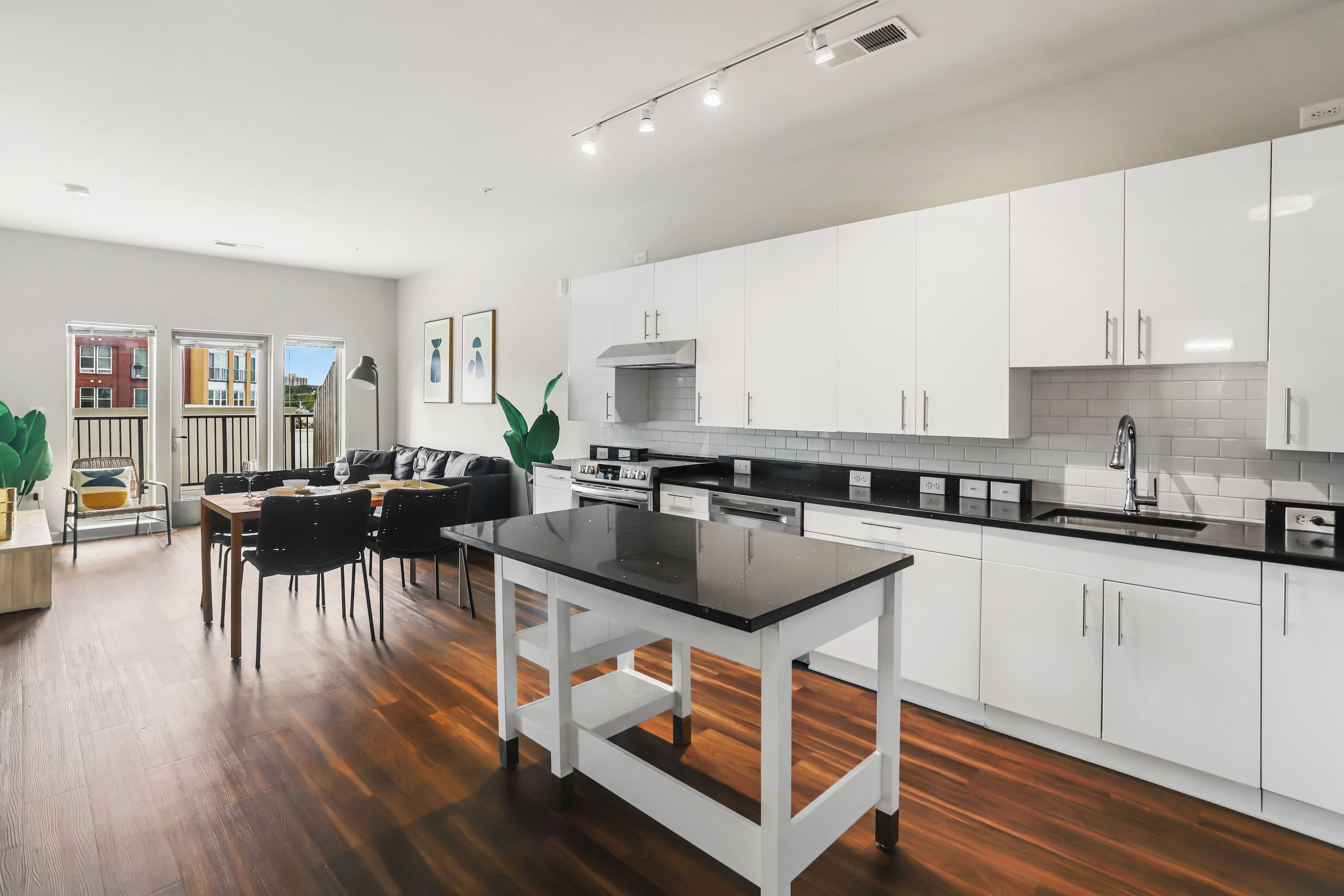 A modern kitchen with white cabinets, a black countertop, and a dining area with a table and chairs.