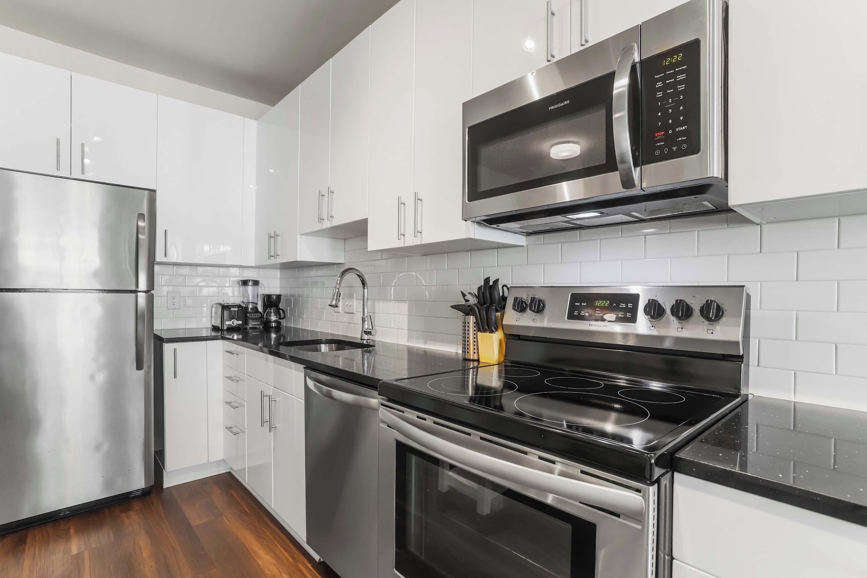 A modern kitchen with stainless steel appliances, white cabinetry, and a black countertop.